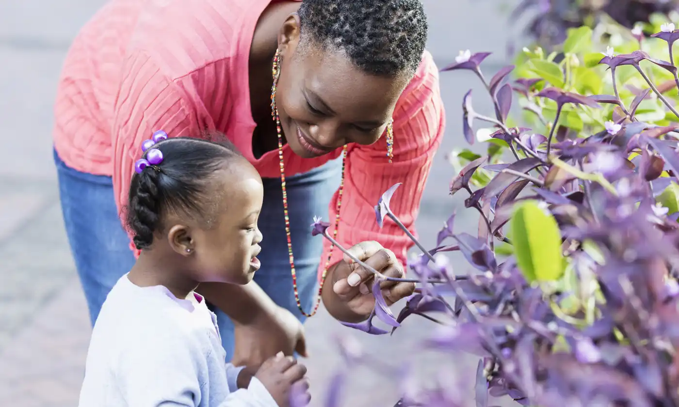 Mother with young daughter bent down to smell flowers